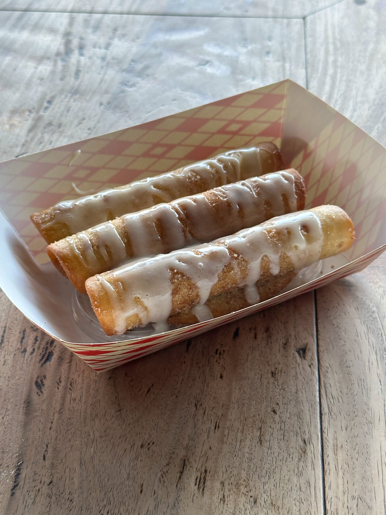 Three glazed pastries with cinnamon sugar in a paper tray.