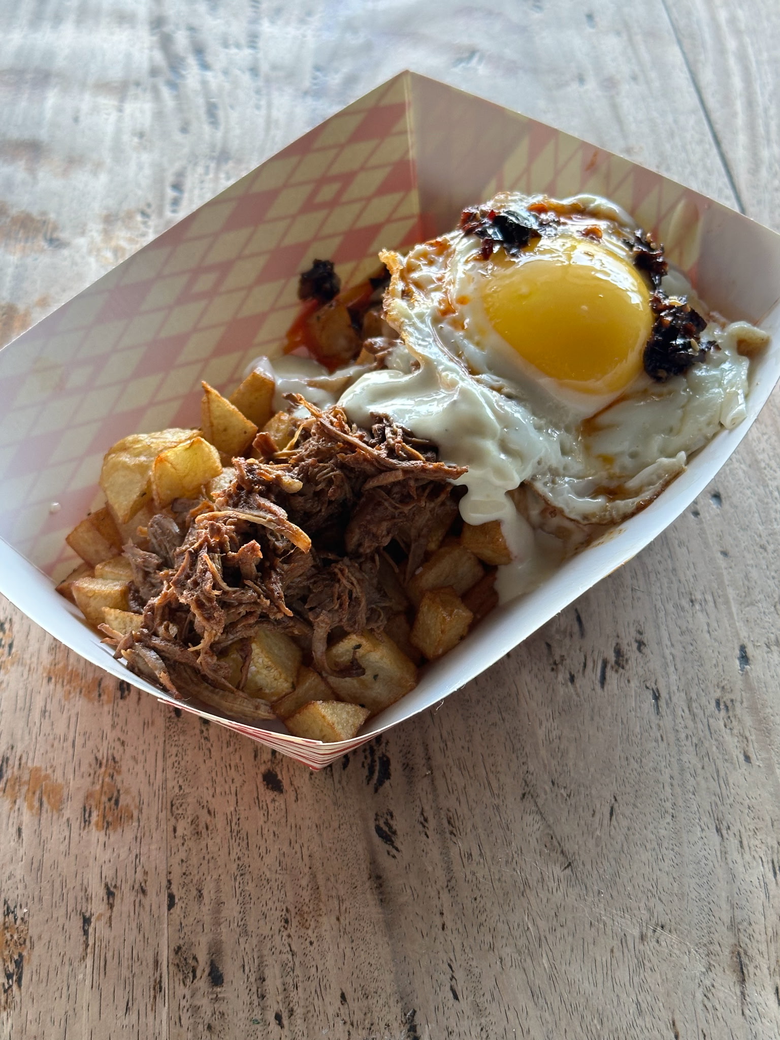 Fried potatoes, pulled meat, sunny-side egg, and a dark topping in a tray.