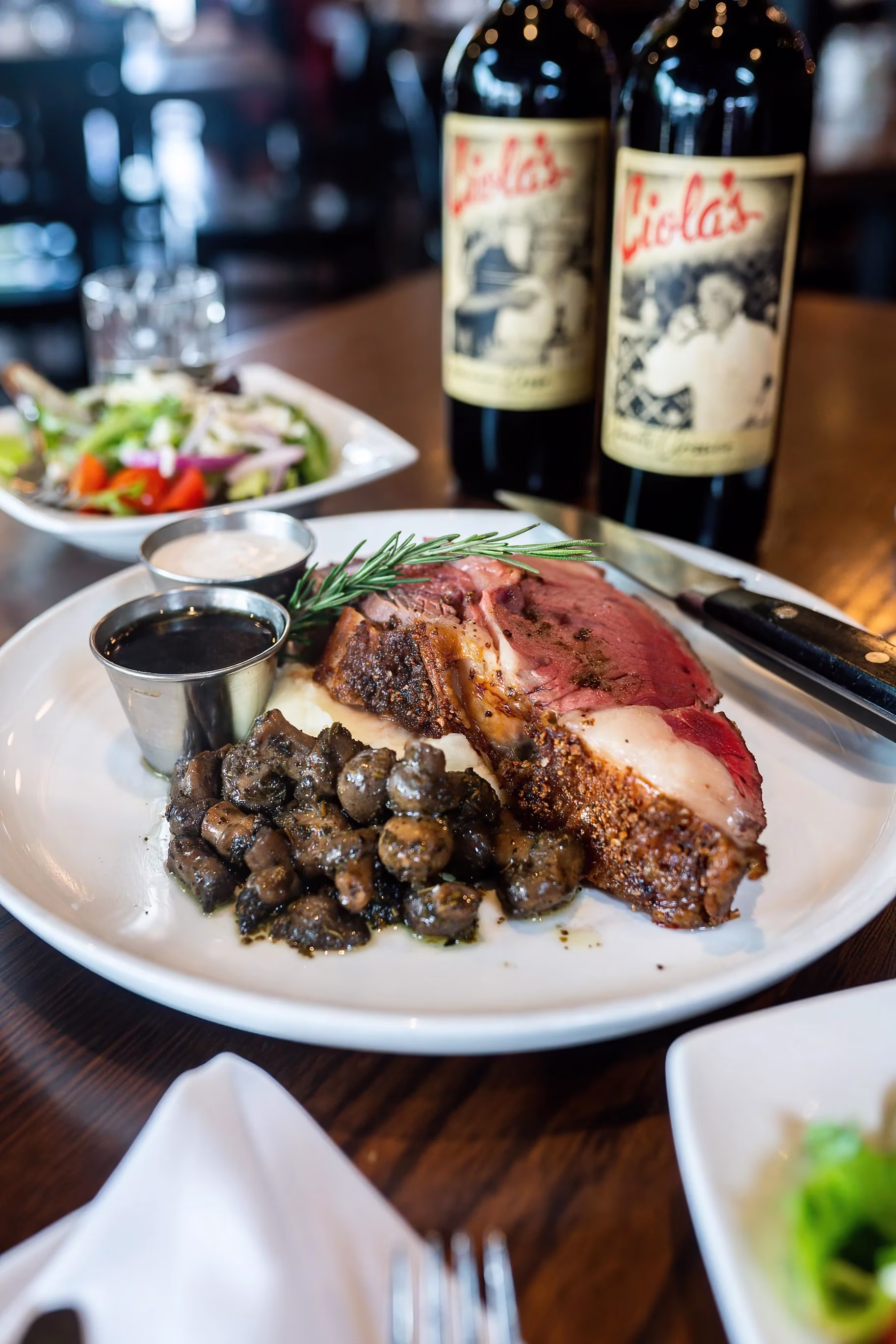Prime rib, mushrooms, sauces, salad, and Ciola's wine bottles.