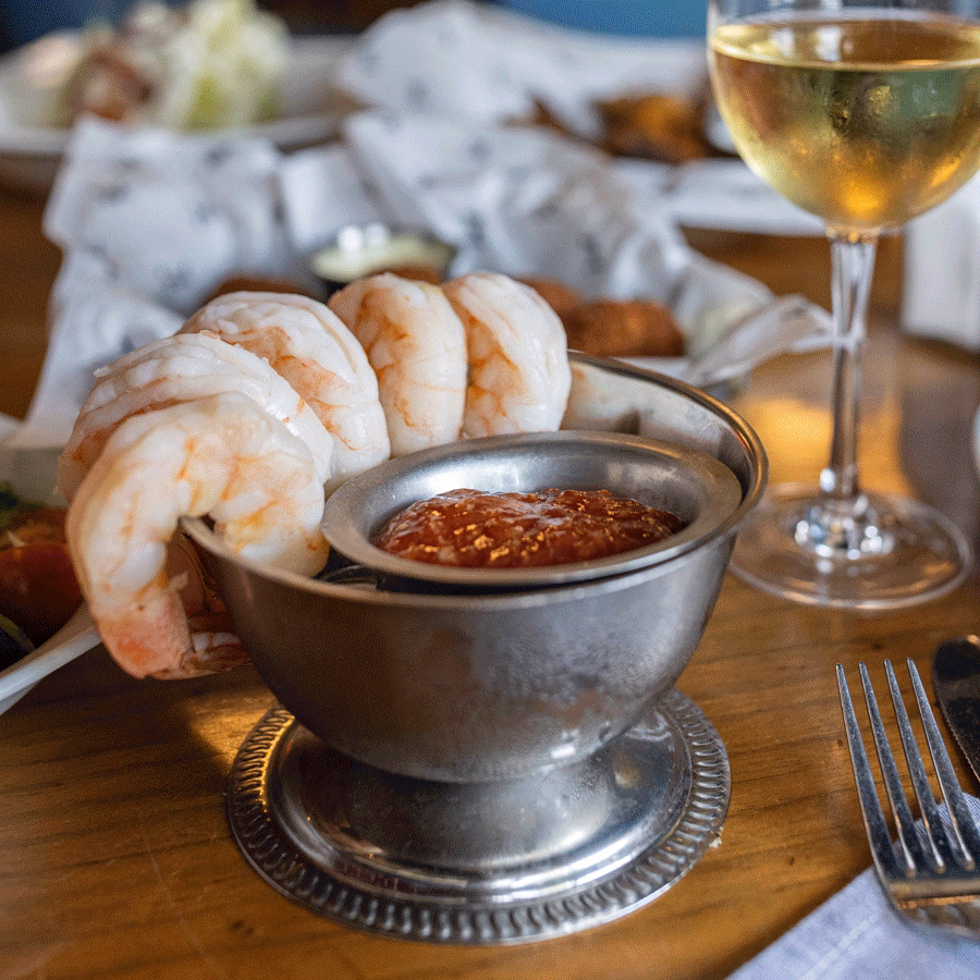 Shrimp cocktail in a metal bowl with sauce and white wine.