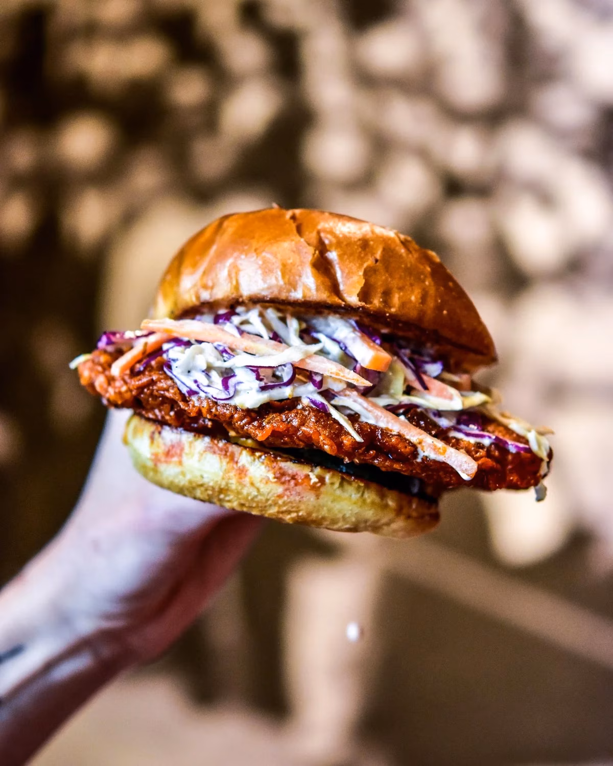 Hand holding a fried patty sandwich with red sauce and coleslaw.