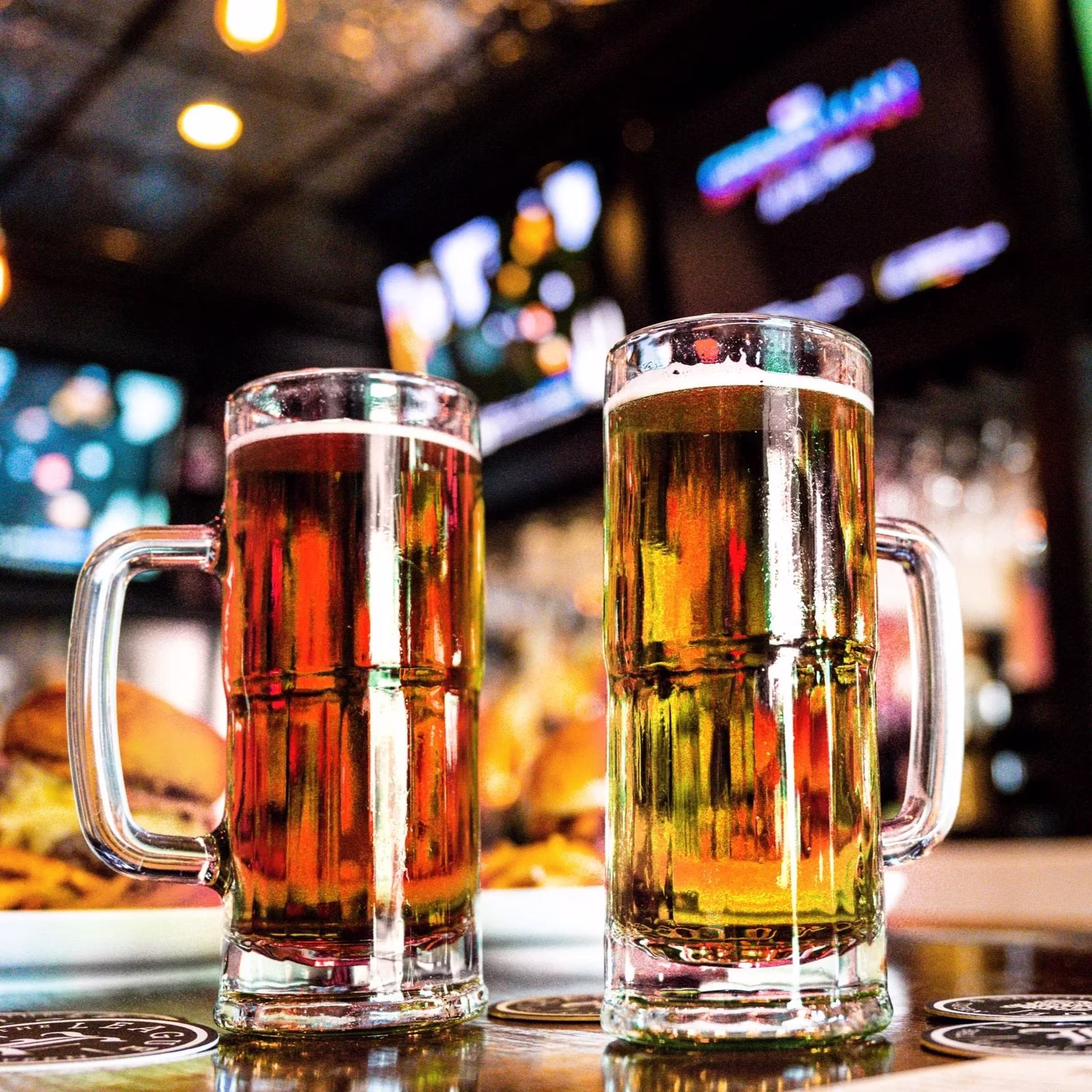 Two full beer mugs on a table at a bar.