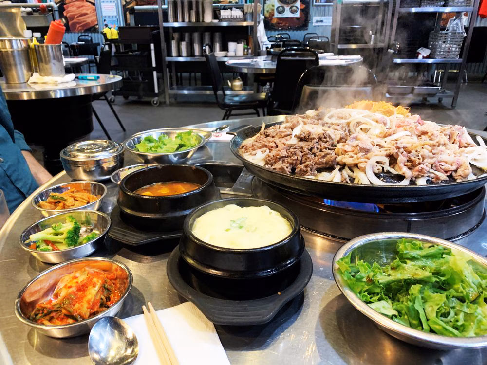 Korean BBQ table with meat and onions cooking, surrounded by banchan.