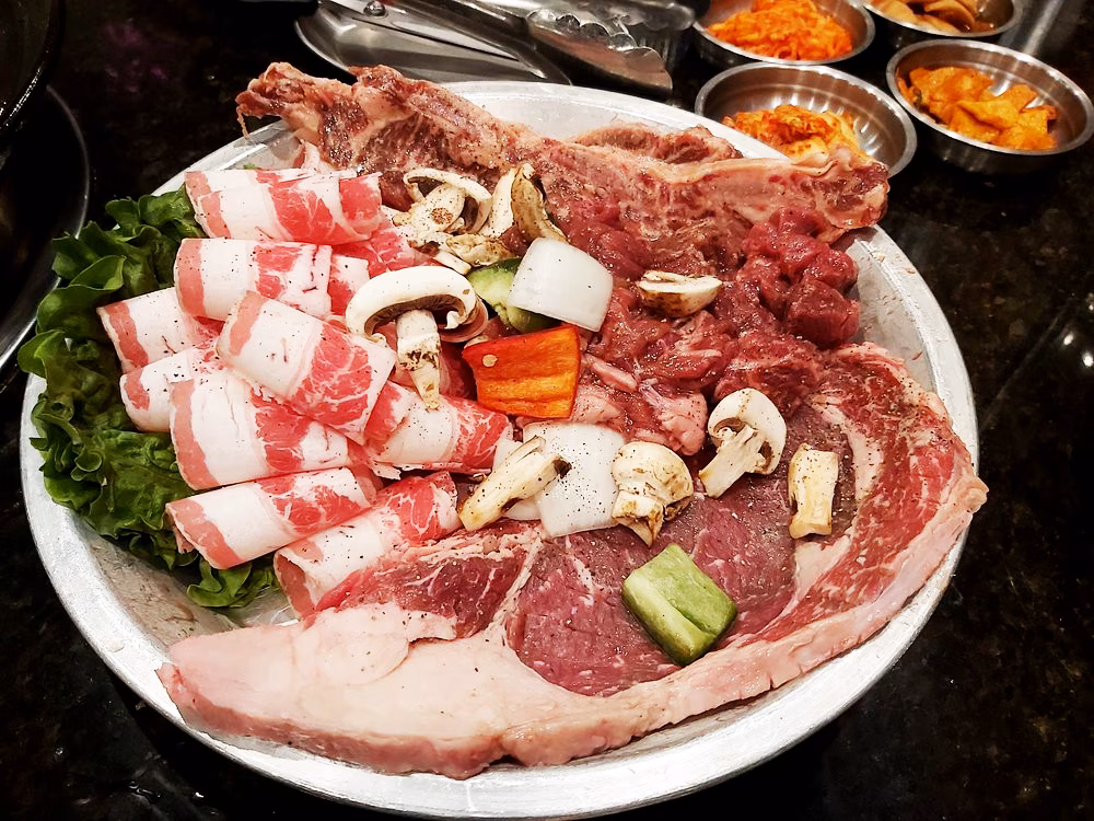 Raw beef slices, steak, vegetables, and mushrooms on a large platter.