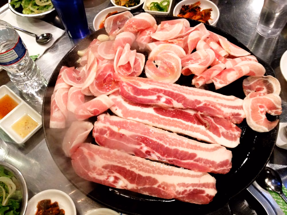 Raw pork belly slices and rolls steaming on a grill.