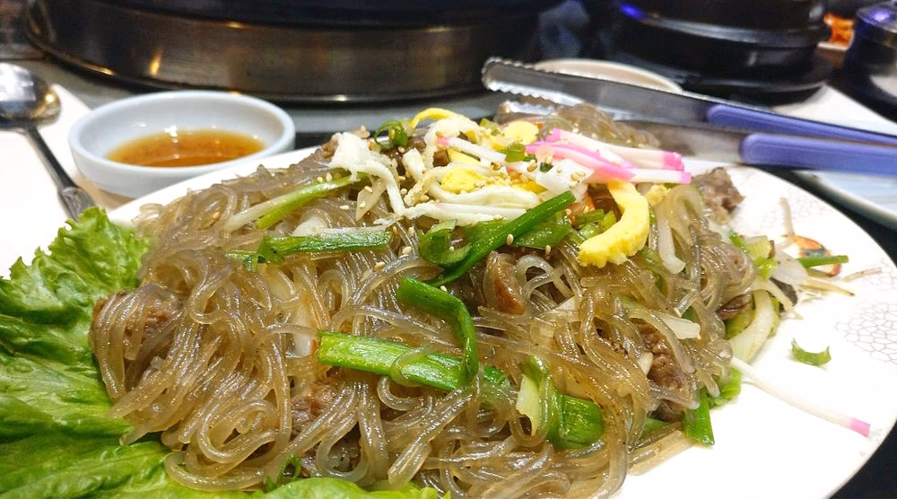 Plate of Korean japchae, glass noodles with beef, vegetables, and egg.