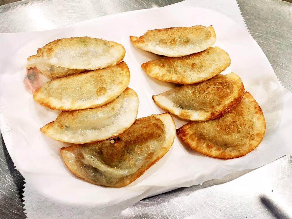 Several golden-brown fried crescent-shaped dumplings on white paper.