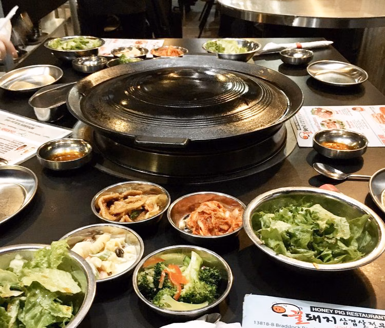 Korean BBQ table with large central grill and many side dishes.