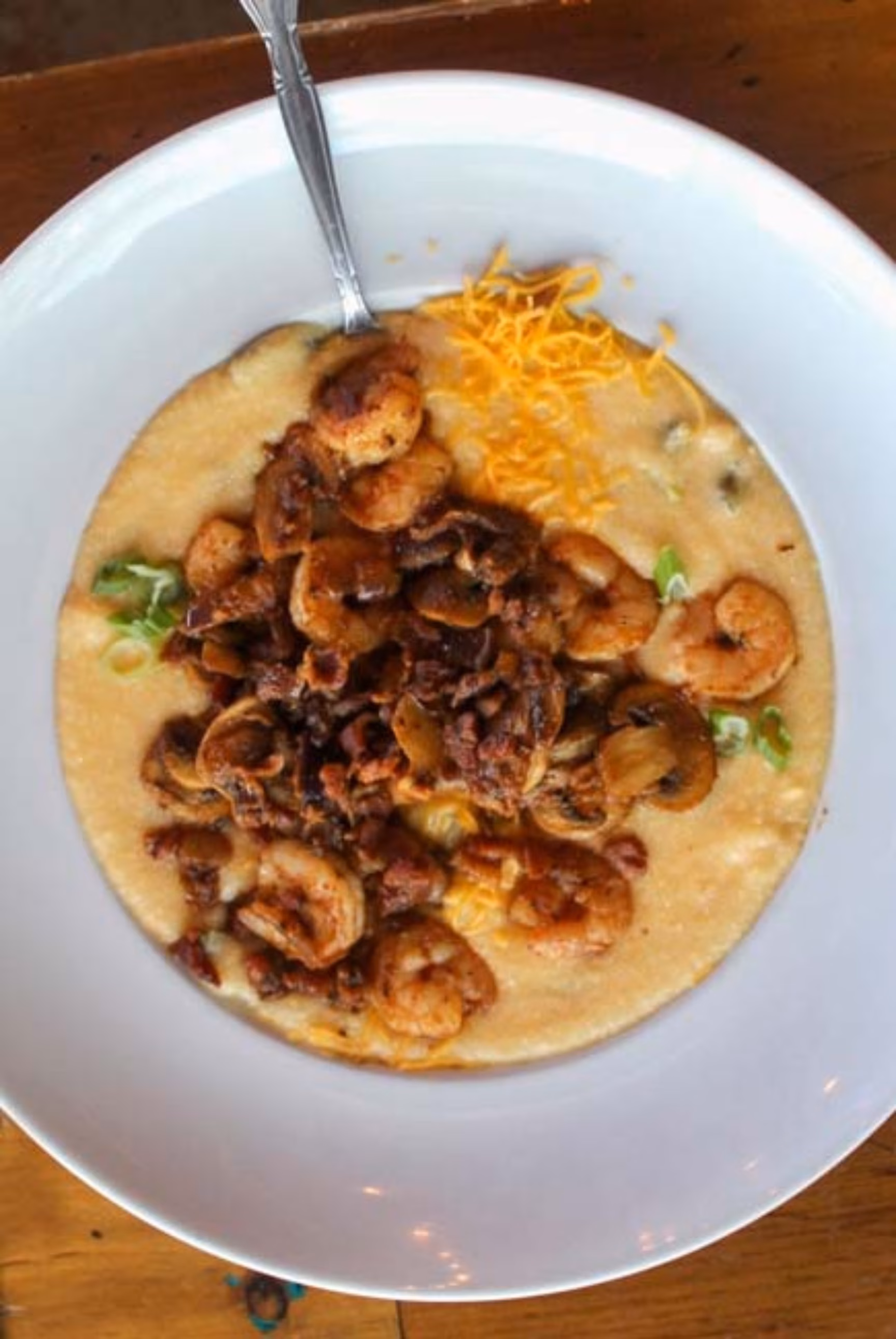 Bowl of shrimp and grits with mushrooms, bacon, and shredded cheese.