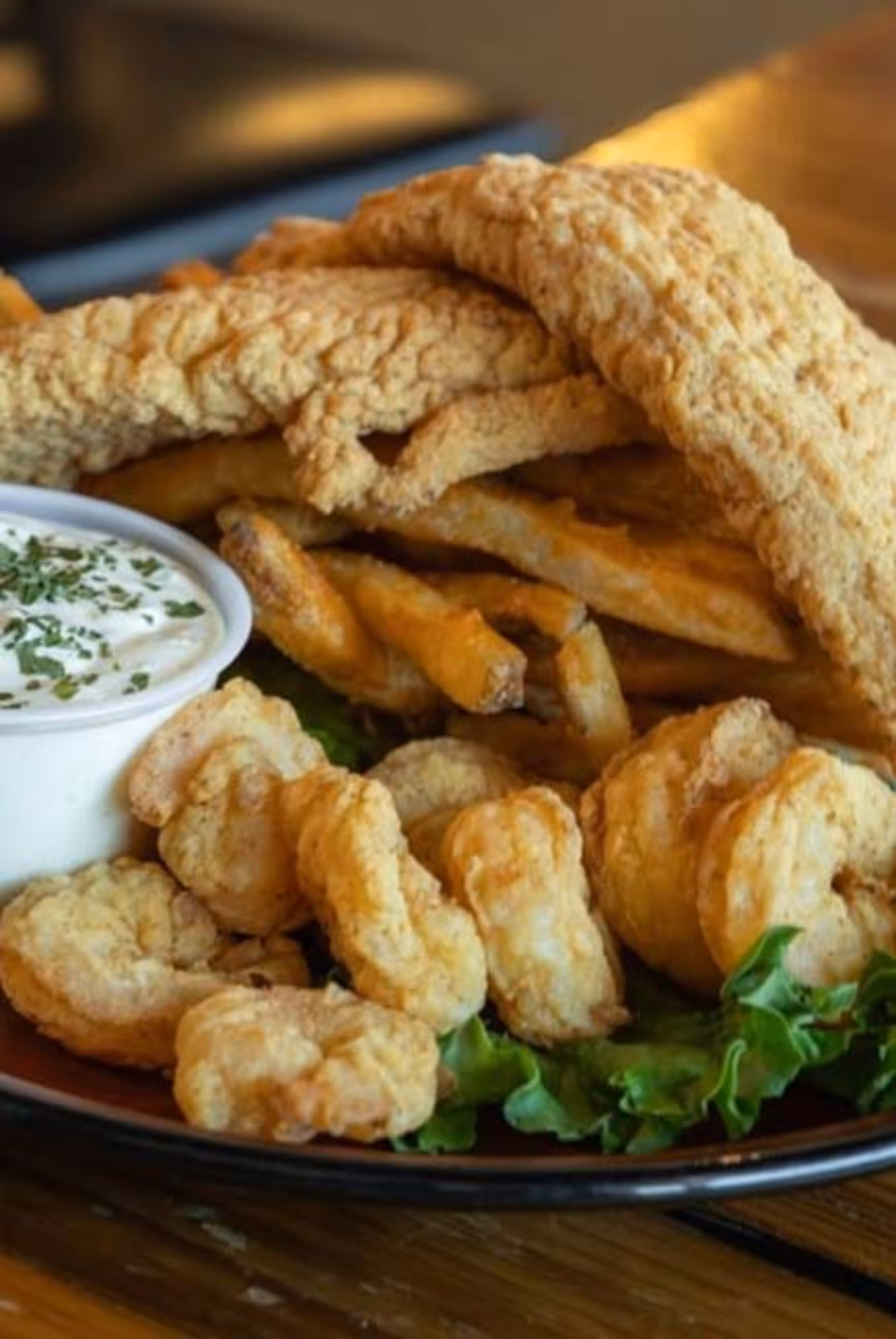 Fried fish, shrimp, and fries with dipping sauce on a plate.