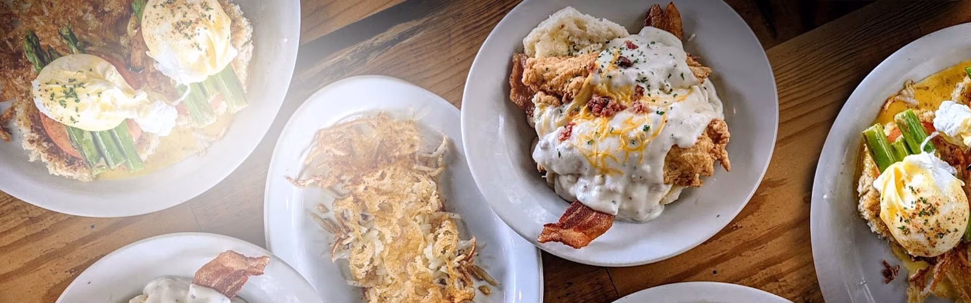 Plates of eggs benedict, fried chicken, and hash browns on a table.