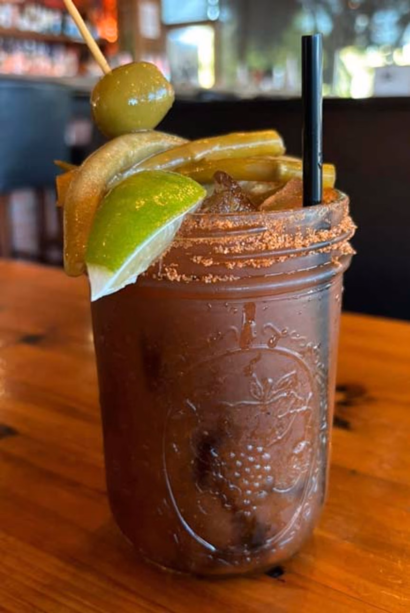 Bloody Mary cocktail in a mason jar with olive, lime, pickles.
