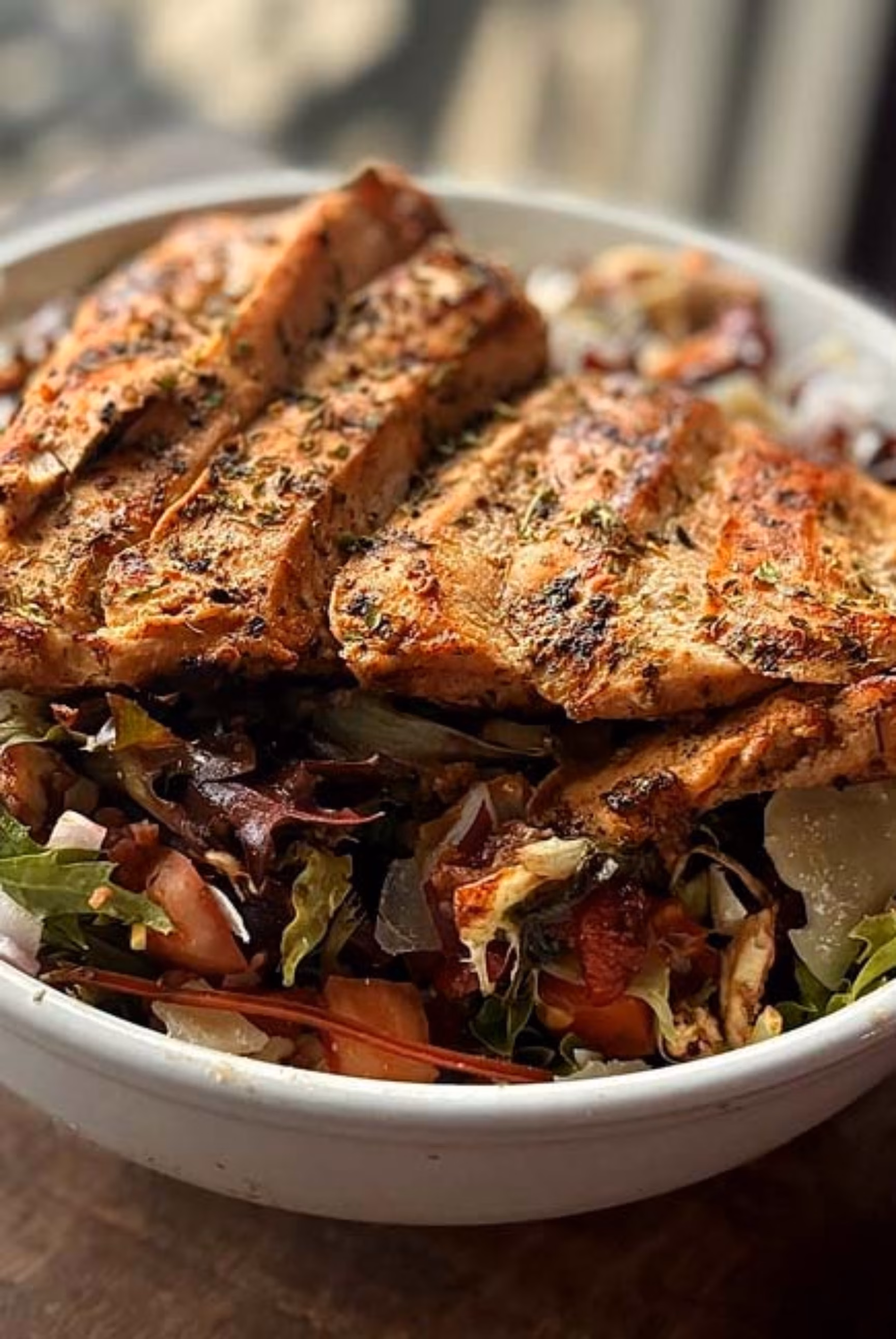 Slices of seasoned grilled chicken breast topping a mixed green salad.