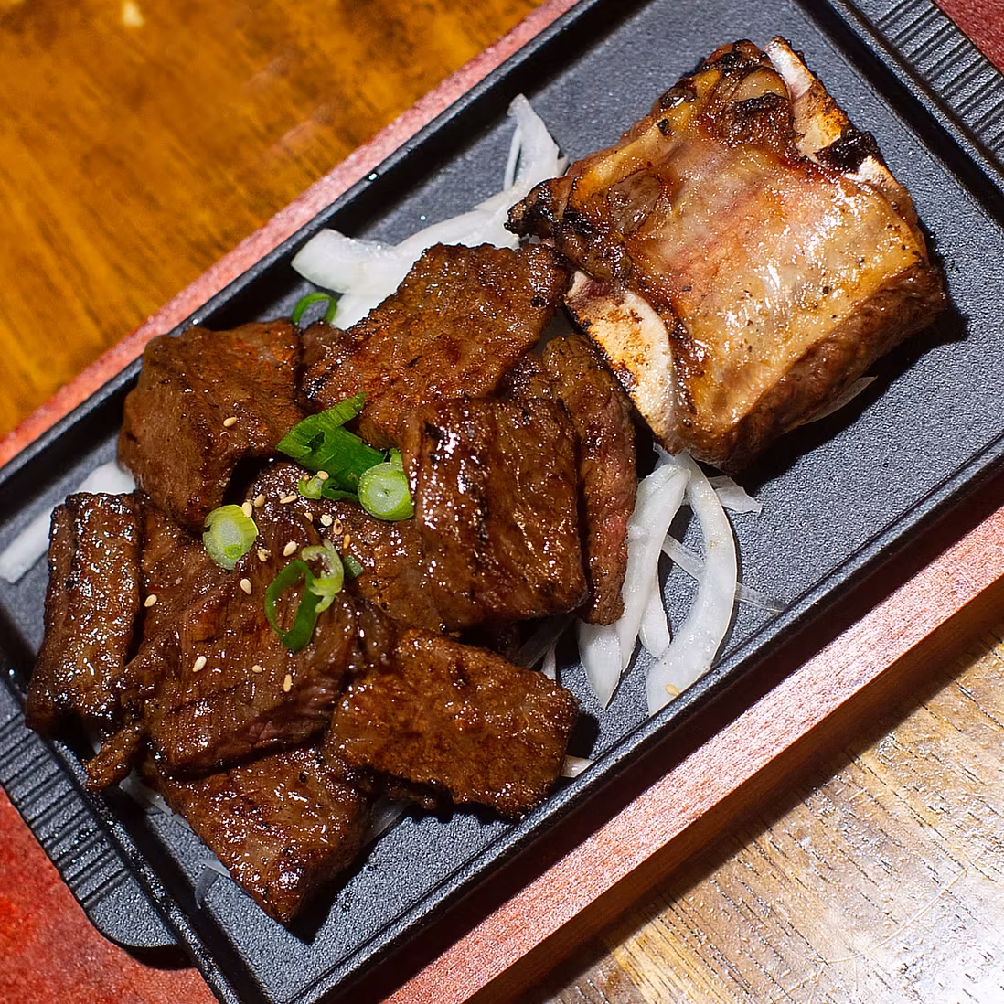 Grilled beef pieces and a bone-in rib with onions on a platter.