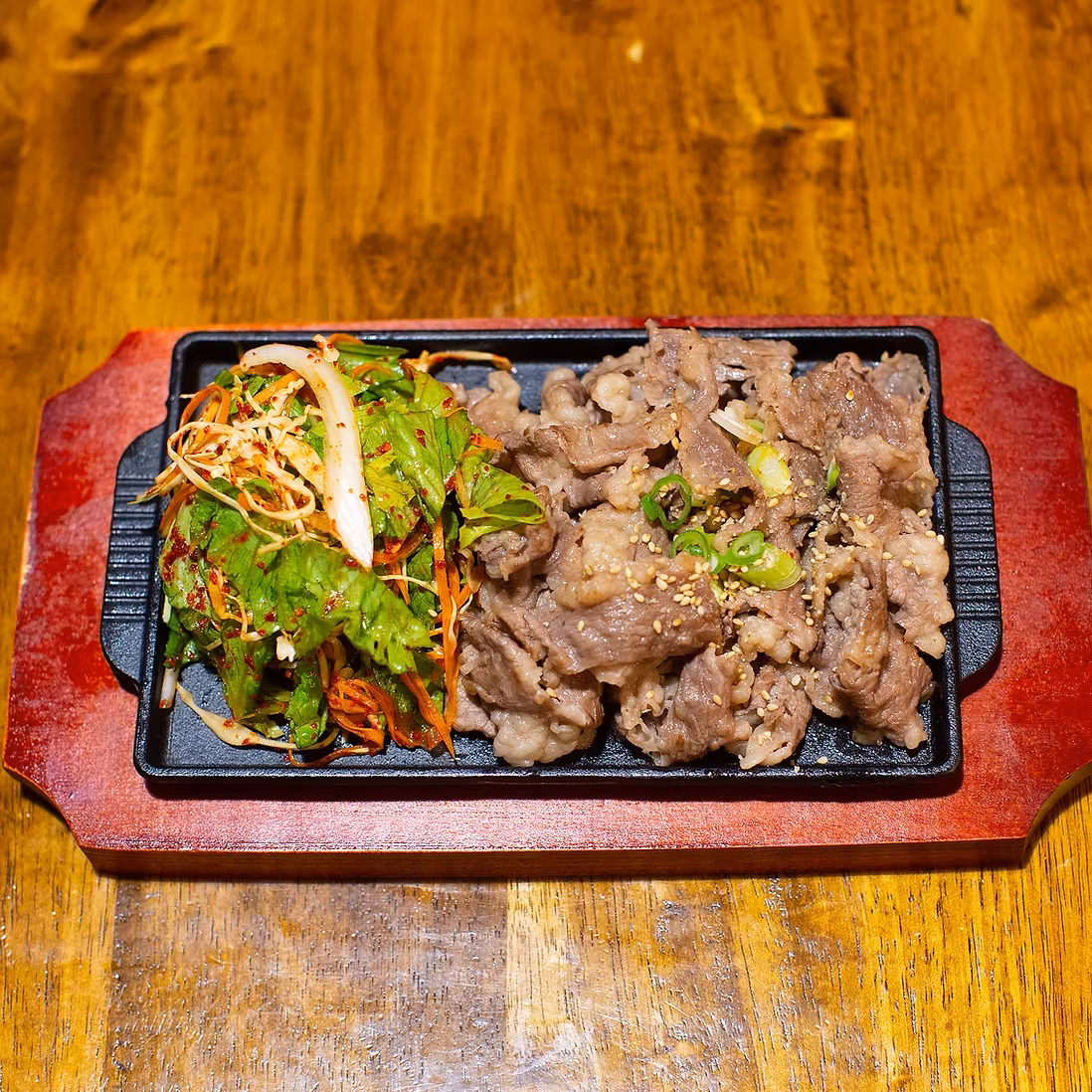 Cooked sliced meat and fresh lettuce salad on a cast iron platter.