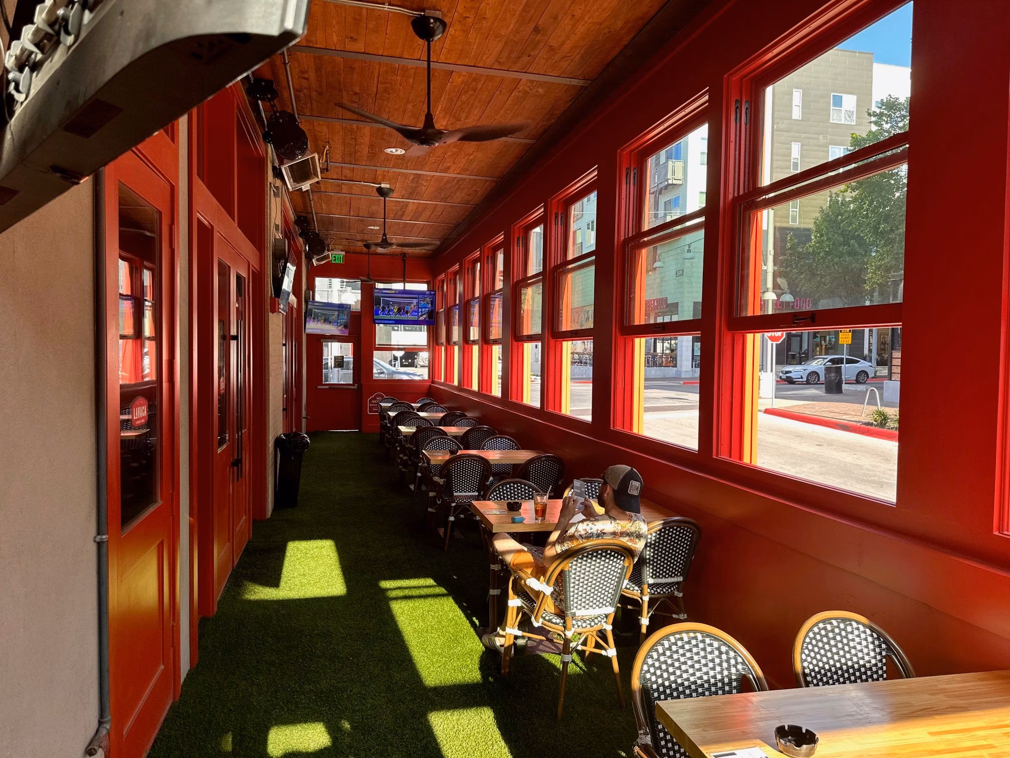 Red-framed patio with artificial grass, tables, and a person reading.