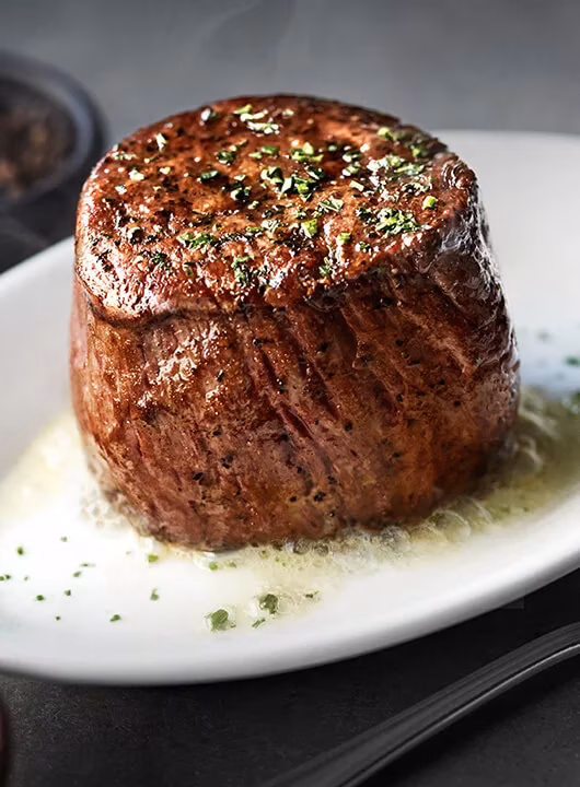 Thick, seared beef steak topped with herbs, resting in melted butter.