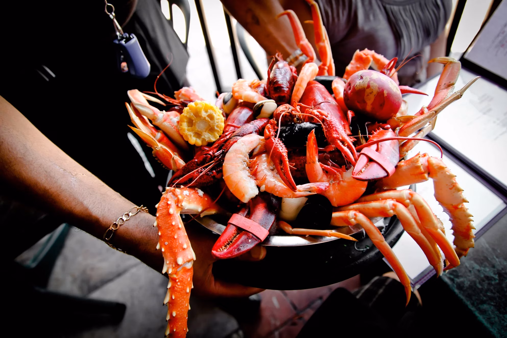 Person holds a large platter of cooked lobster, crab, shrimp, and corn.