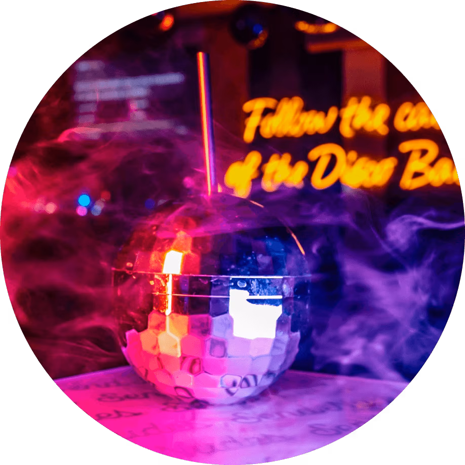 Smoky disco ball drink with straw and glowing neon sign.