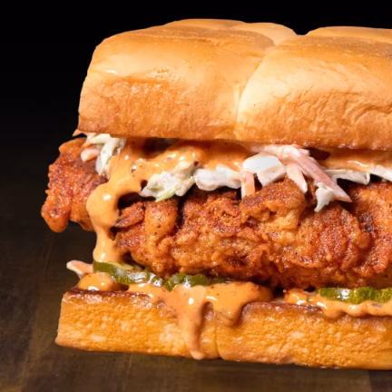 Fried chicken sandwich with coleslaw, sauce, and pickles on a bun.