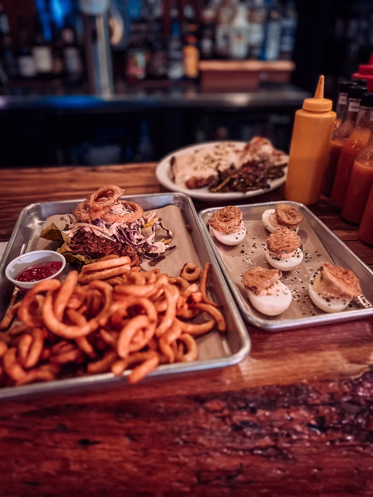 Platters with a sandwich, curly fries, and deviled eggs on a counter.