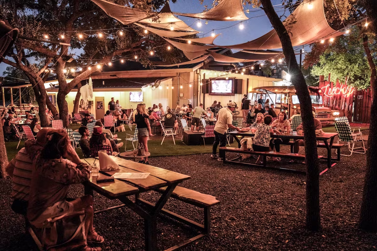 People dine outdoors under string lights and shade sails at night.