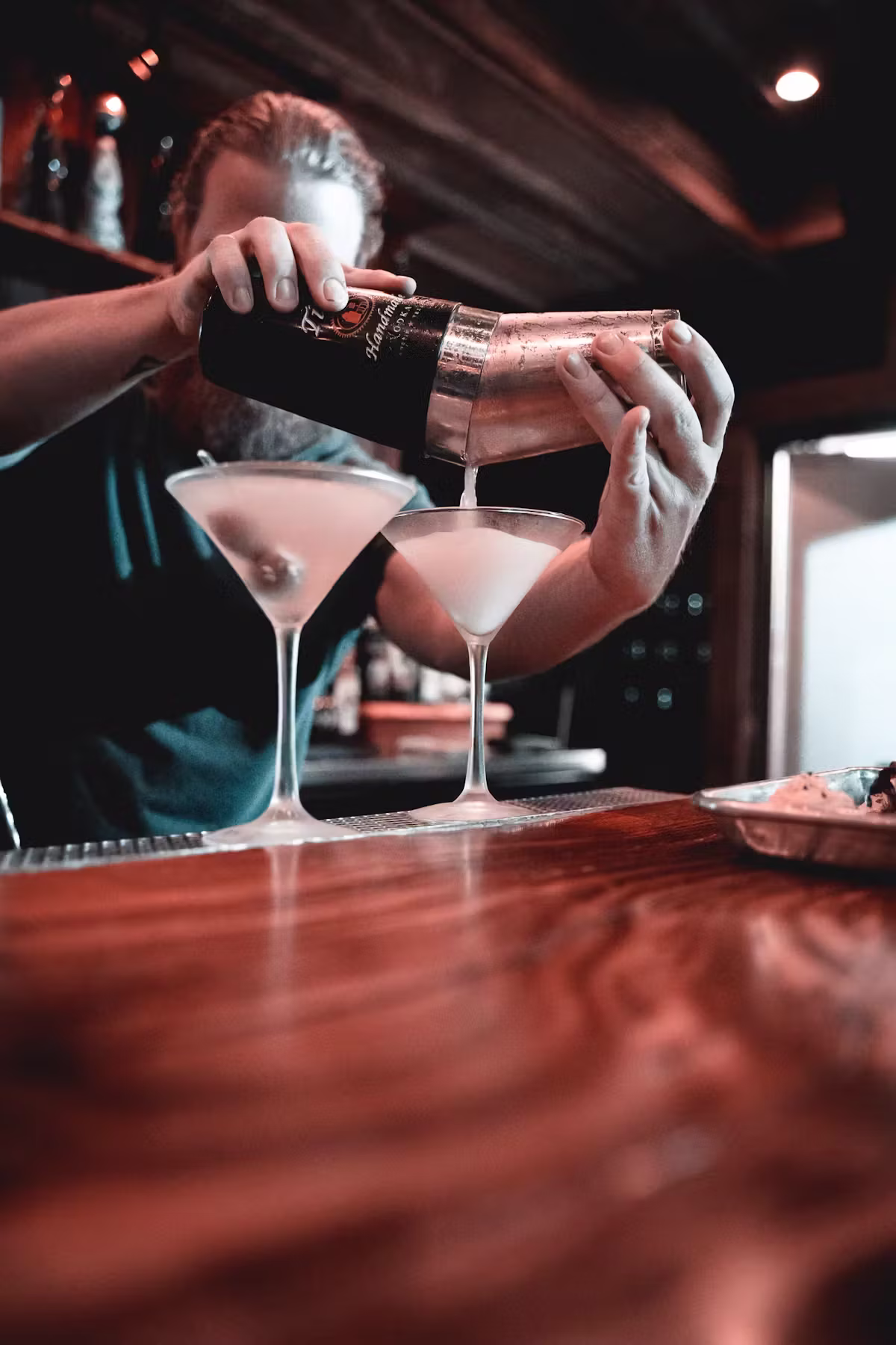 Bartender pouring cocktail from shaker into two martini glasses.