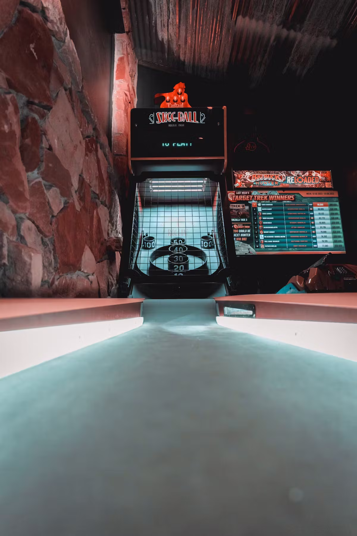 Skee-Ball machine and Big Buck Hunter game in a dark arcade.