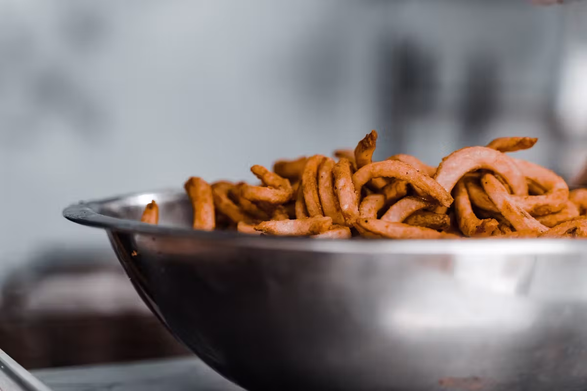 Large metal bowl full of golden, seasoned curly fries.