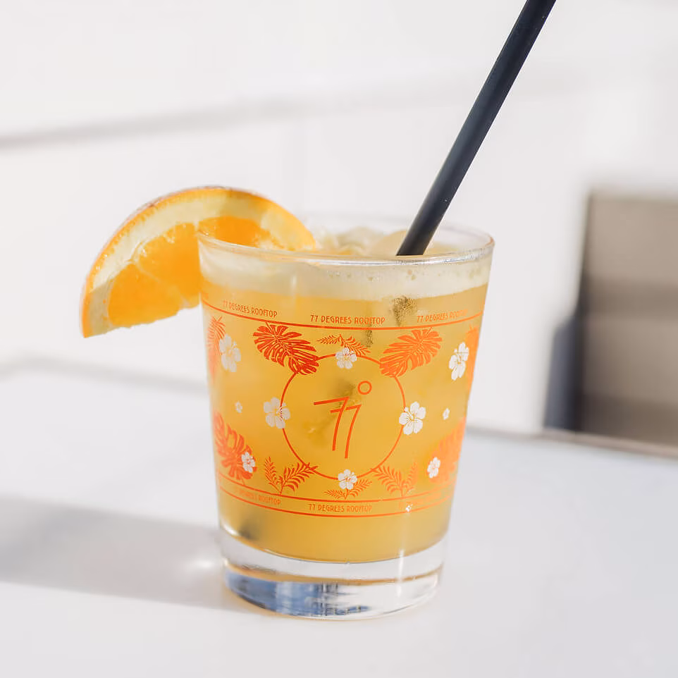 Orange drink in a branded glass with an orange slice and straw.