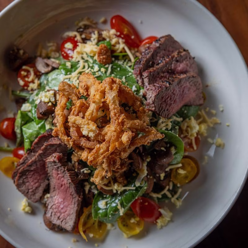 Sliced steak salad with crispy onions, greens, tomatoes, and cheese.