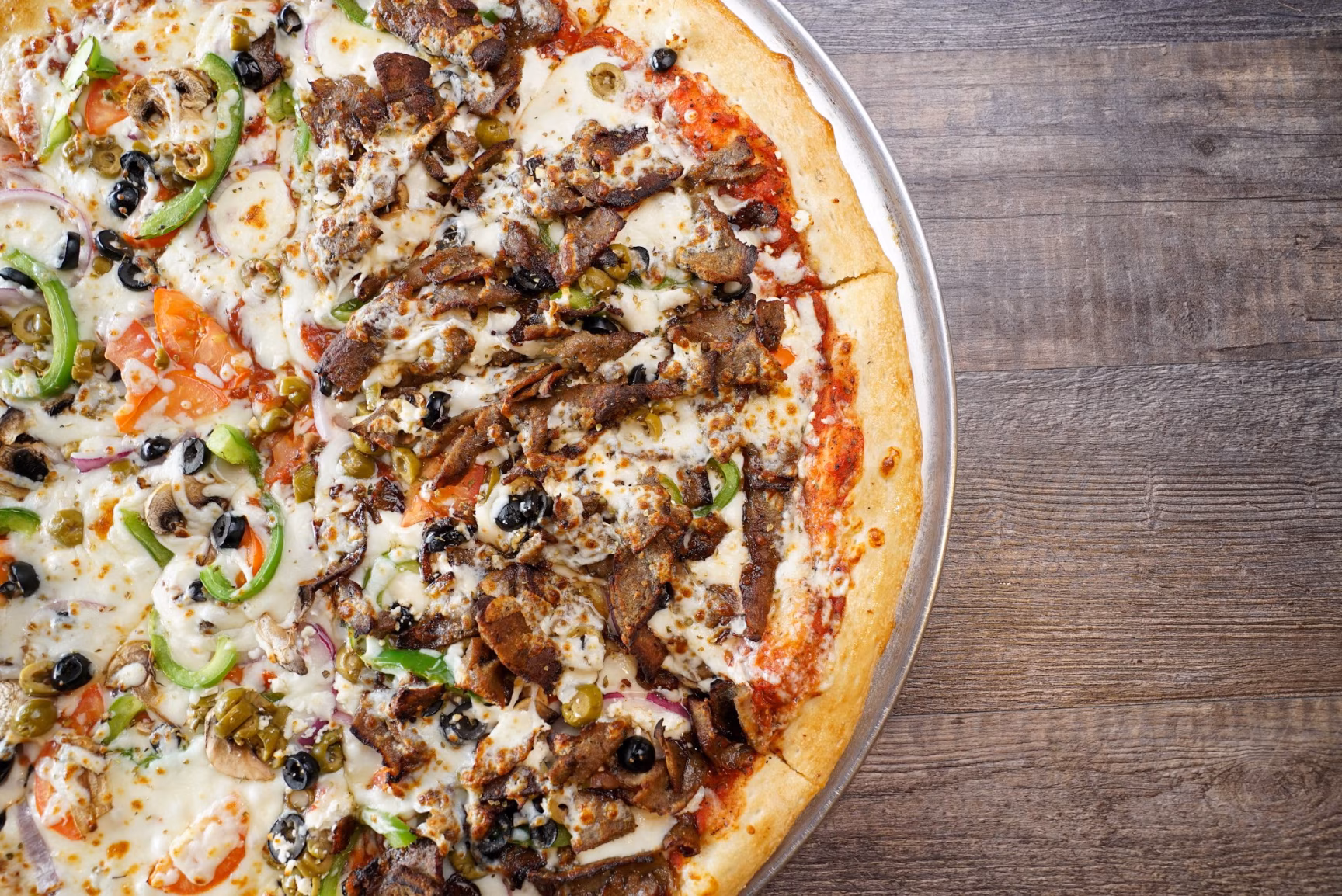 Large pizza on a metal tray, half meat, half vegetable.