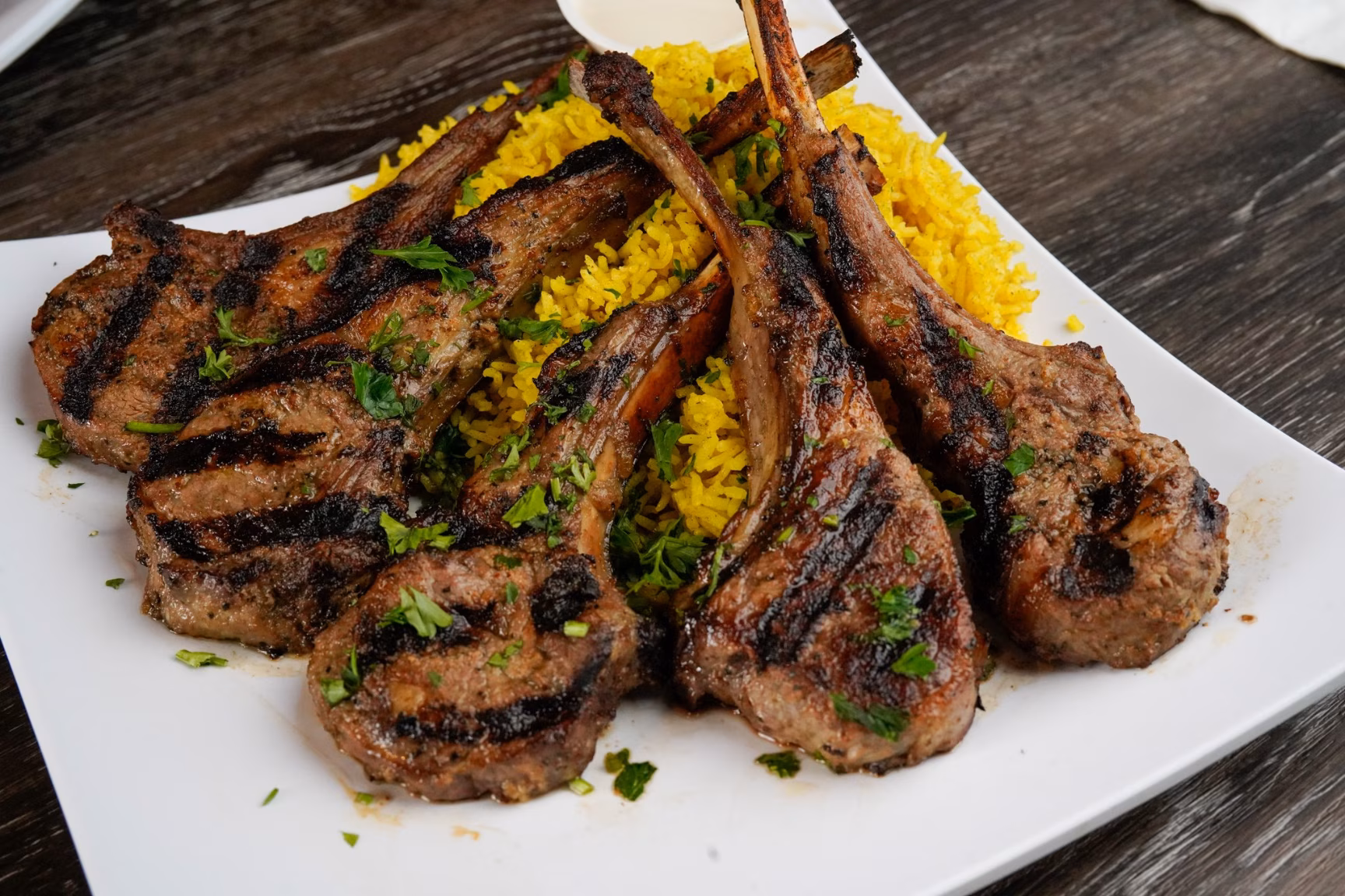 Six grilled lamb chops with yellow rice and parsley on a white plate.