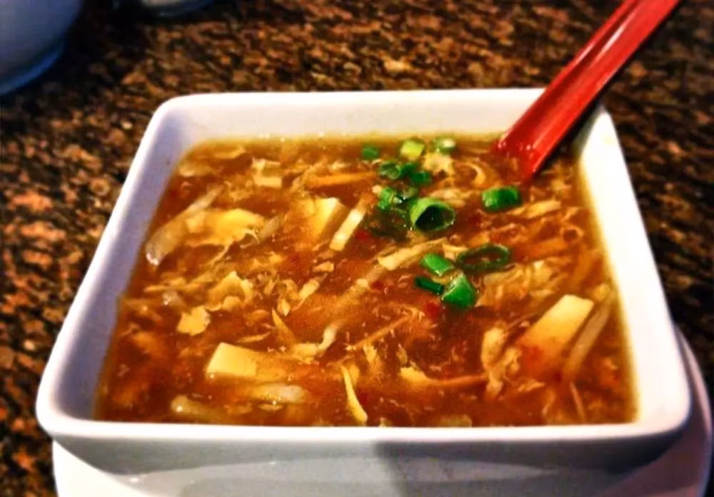 Square bowl of brown soup with chicken, tofu, and green onions.