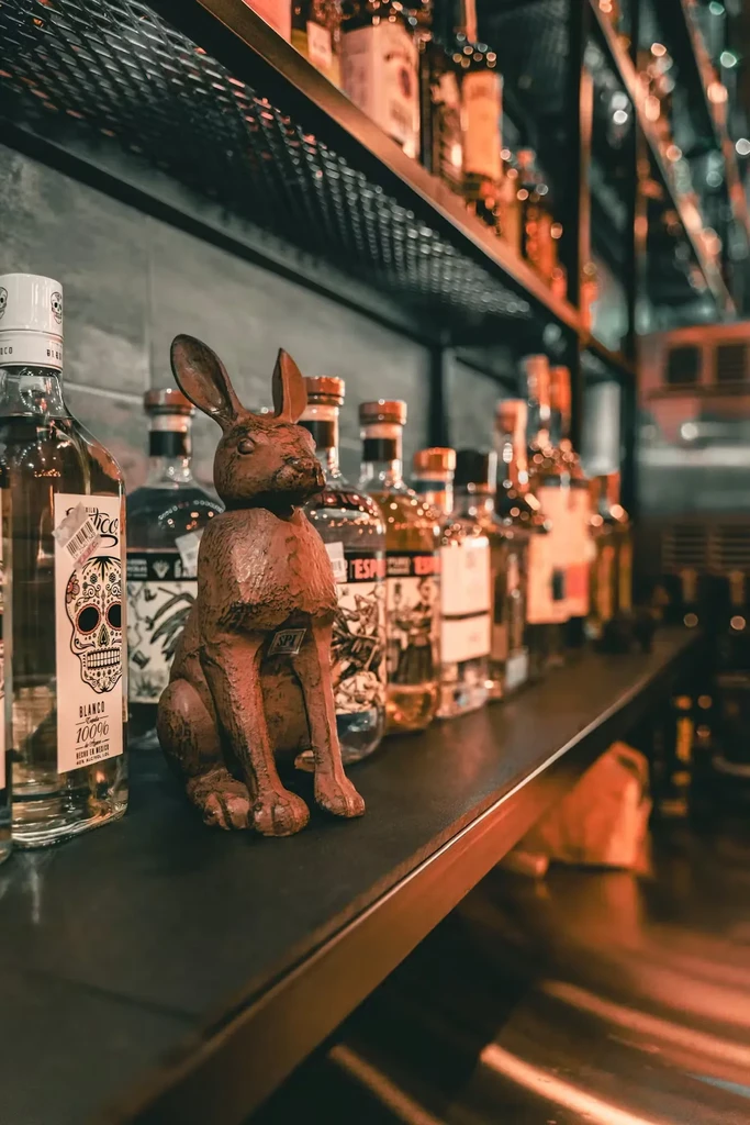 Rustic rabbit figurine on a dark bar shelf with a tequila bottle.