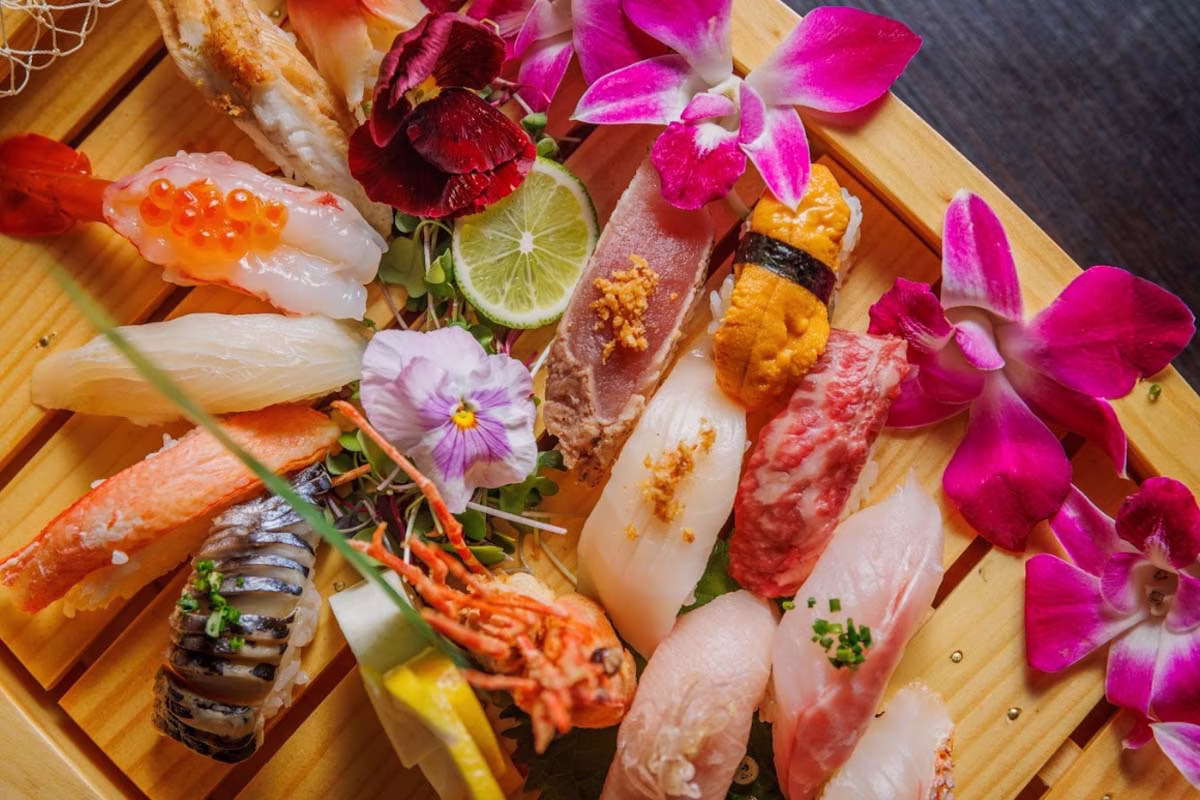 Platter of varied sushi and sashimi with orchids, pansies, and lime.