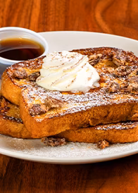 Golden French toast topped with whipped cream, crumbled nuts, and syrup.