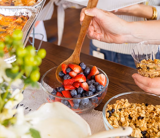 Person scoops mixed berries from a glass bowl with a spoon.