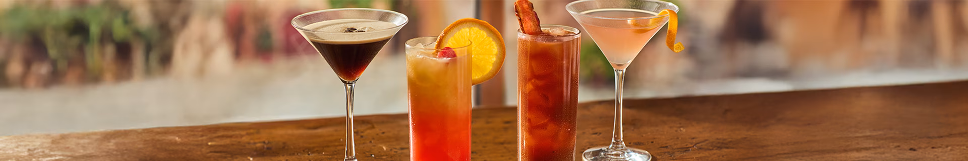 Four varied cocktails on a wooden bar top.