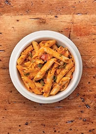 White bowl of penne pasta with red sauce on a wooden surface.