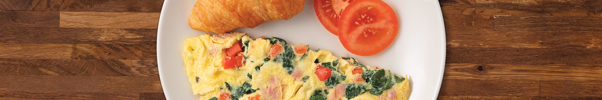 Omelet, croissant, and tomato slices on a white plate.