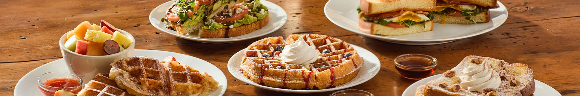 Breakfast spread with waffles, French toast, avocado toast, egg sandwich, fruit.