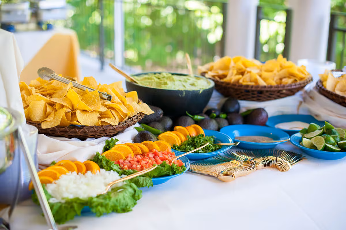 Buffet table with chips, guacamole, fresh salsa, limes, and avocados.