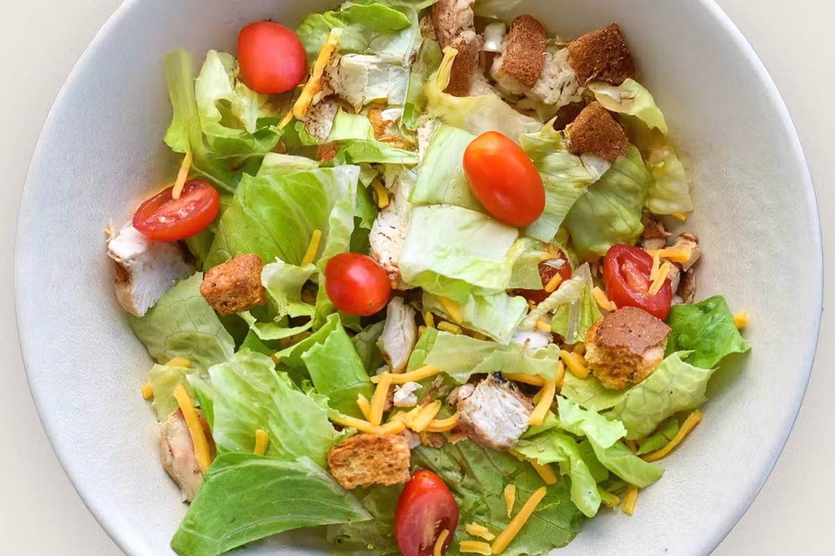 A bowl of green salad with chicken, tomatoes, cheese, and croutons.