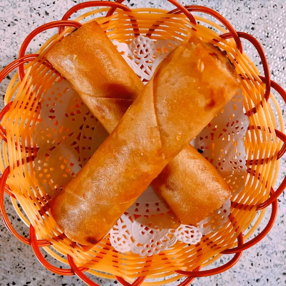 Two golden-brown fried rolls in an orange basket with white doily.