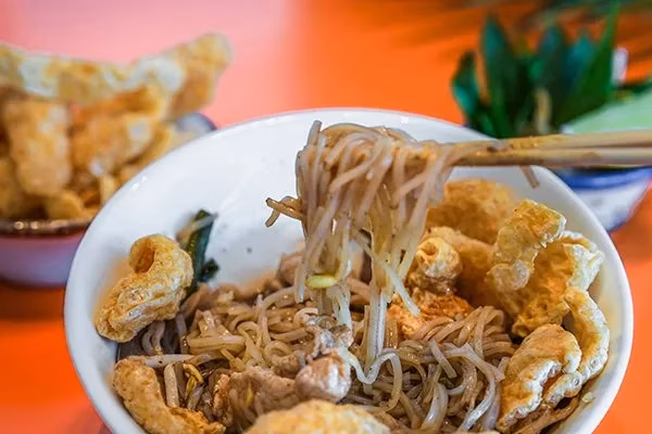 Bowl of noodles with pork rinds, lifted by chopsticks.