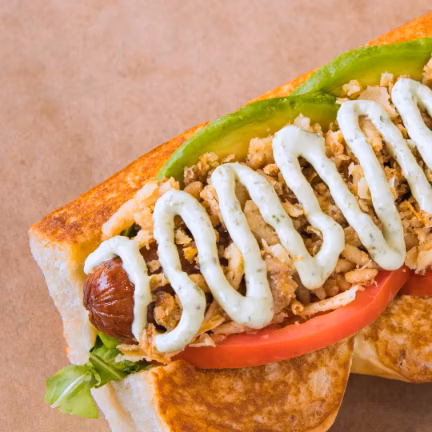 Hot dog with avocado, tomato, crispy onions, and green sauce.