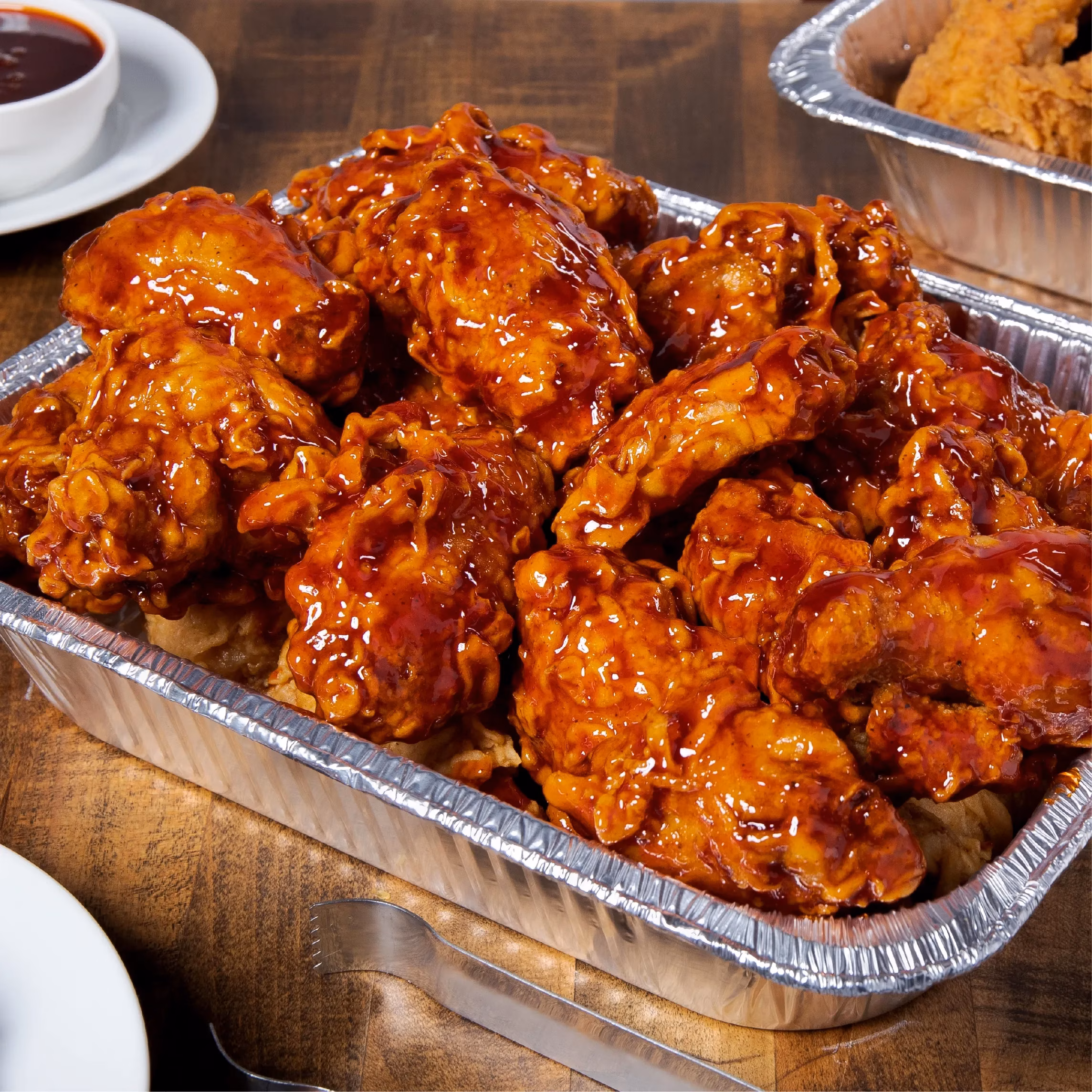 Large foil tray filled with glossy, sauced chicken wings.