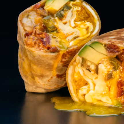 Two sliced burritos filled with eggs, avocado, and dripping cheese sauce.