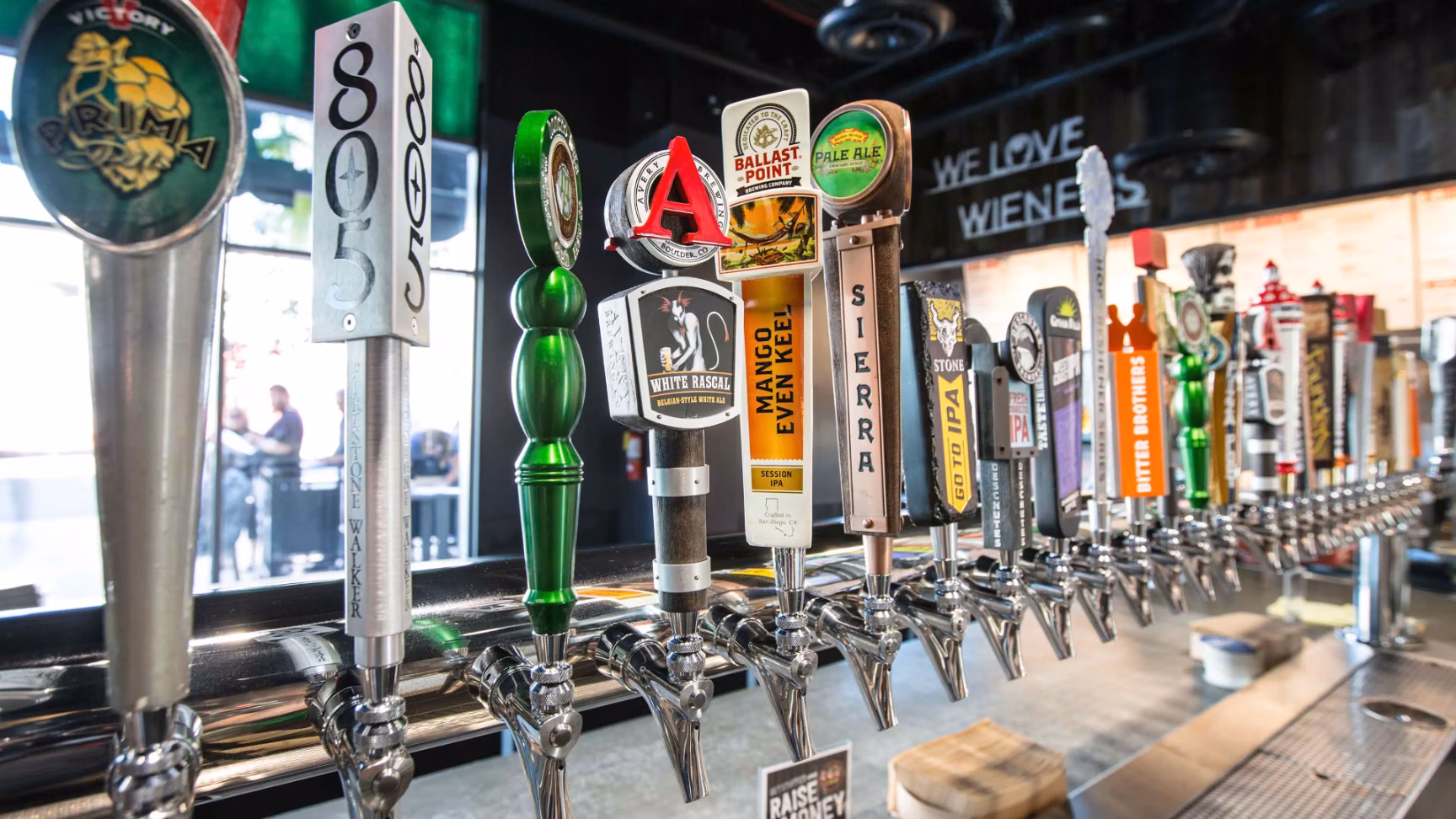 A long row of diverse beer tap handles at a bar.